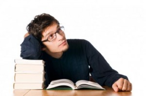 Handsome pensive young man studying on a stack of books on table.
